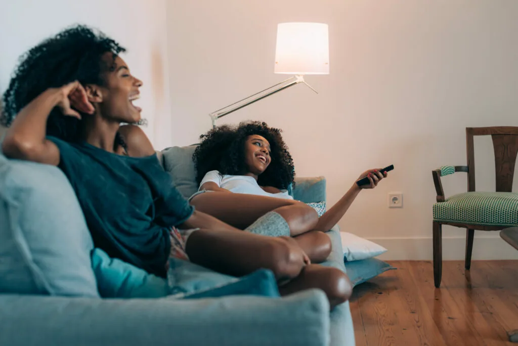 Two people sitting on a couch watching television with a remote control in hand