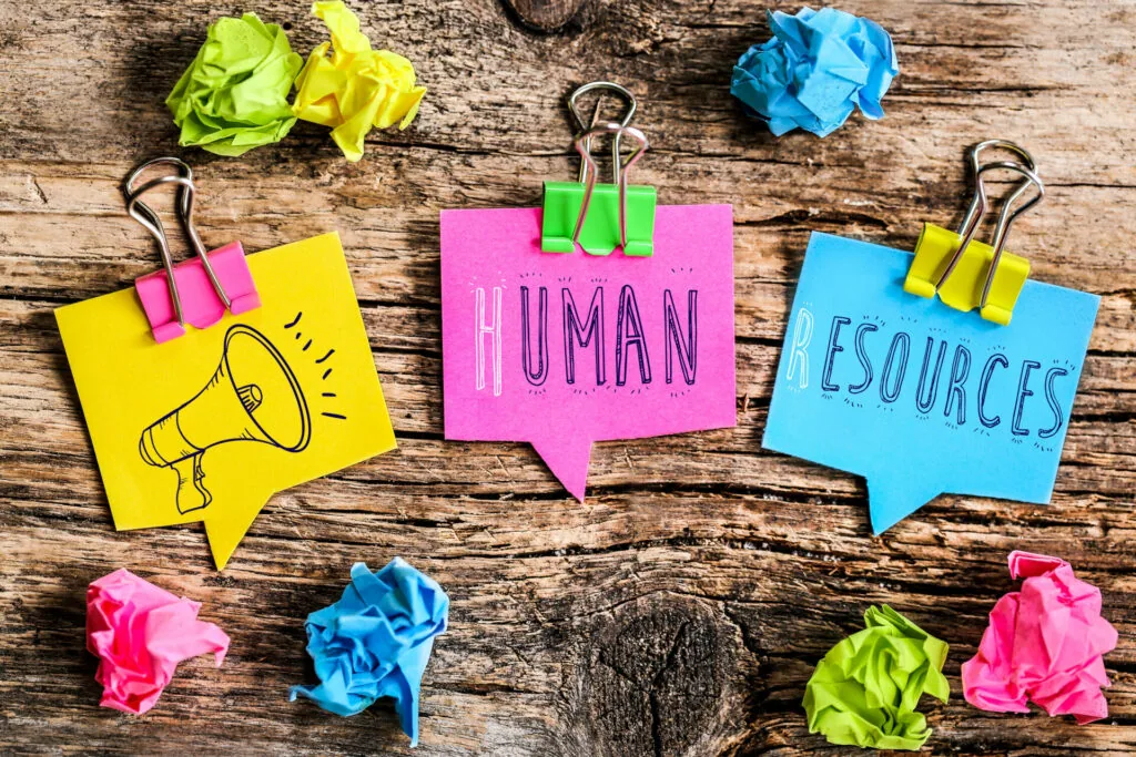 Colorful sticky notes on wooden surface with megaphone, Human Resources text, and crumpled paper balls held by binder clips