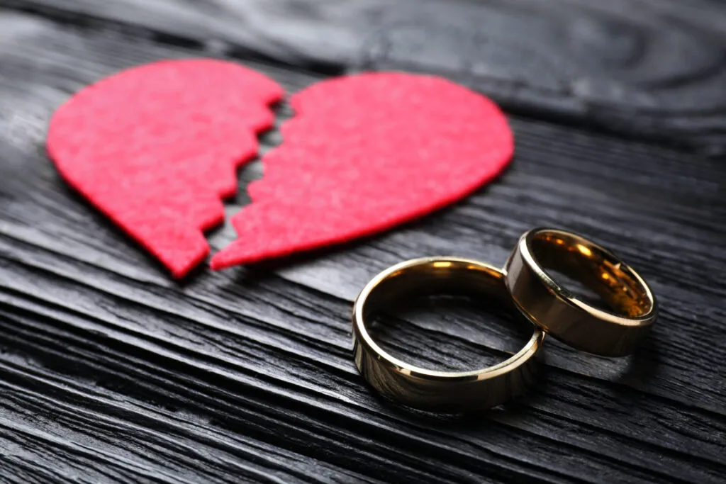 Two gold wedding rings placed next to a broken pink paper heart on dark wood surface