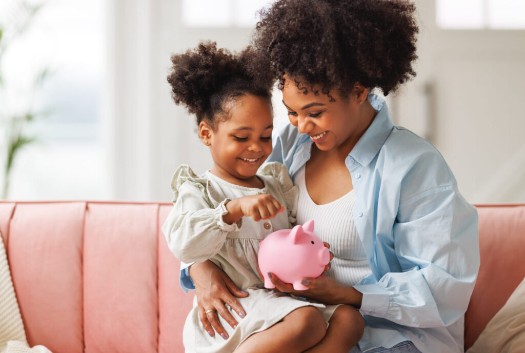 financial education. african american family, mother and child daughter with pig piggy bank counting savings at home on sofa